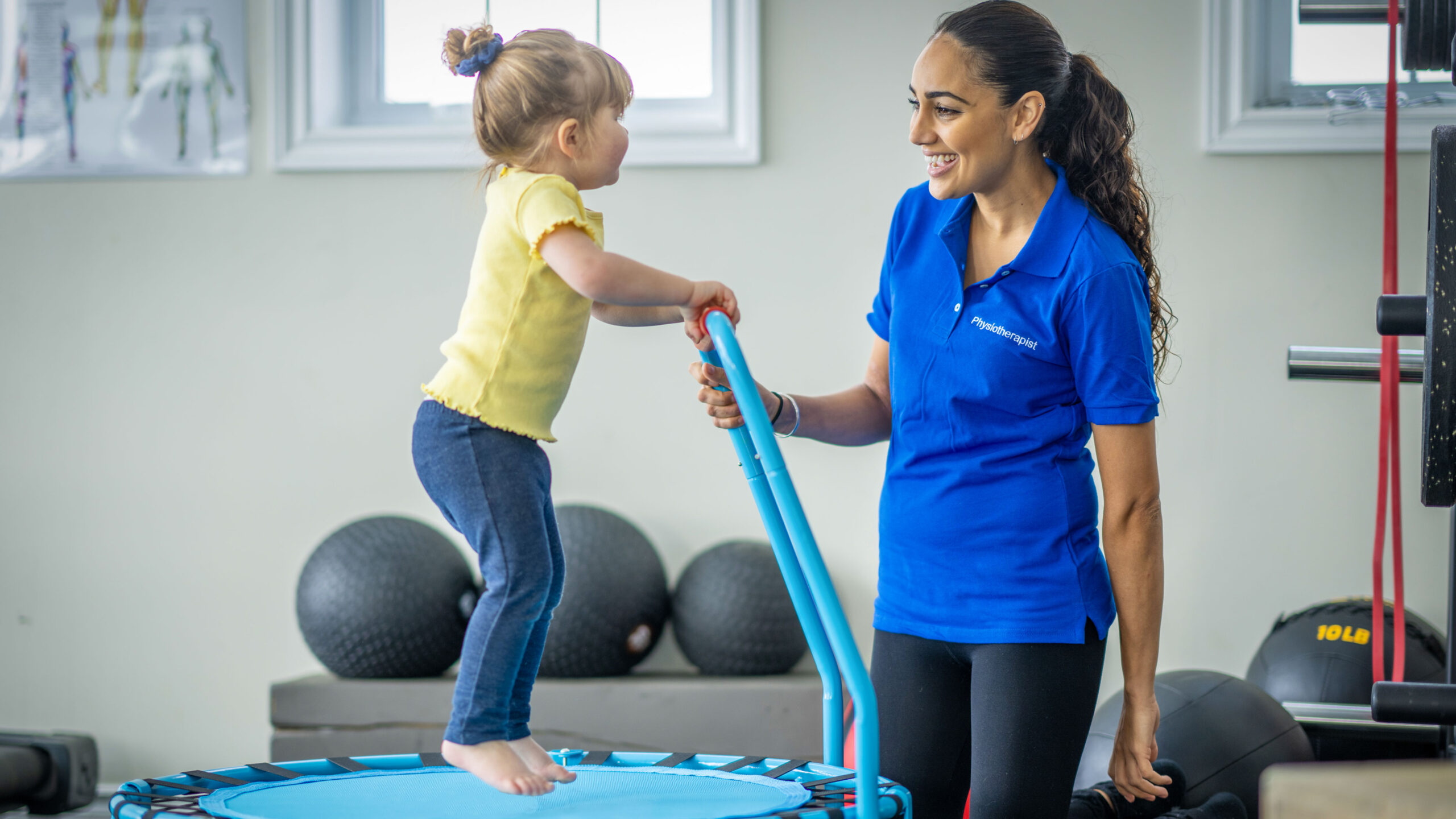 Little girl guided by a therapist jumping on a trampoline