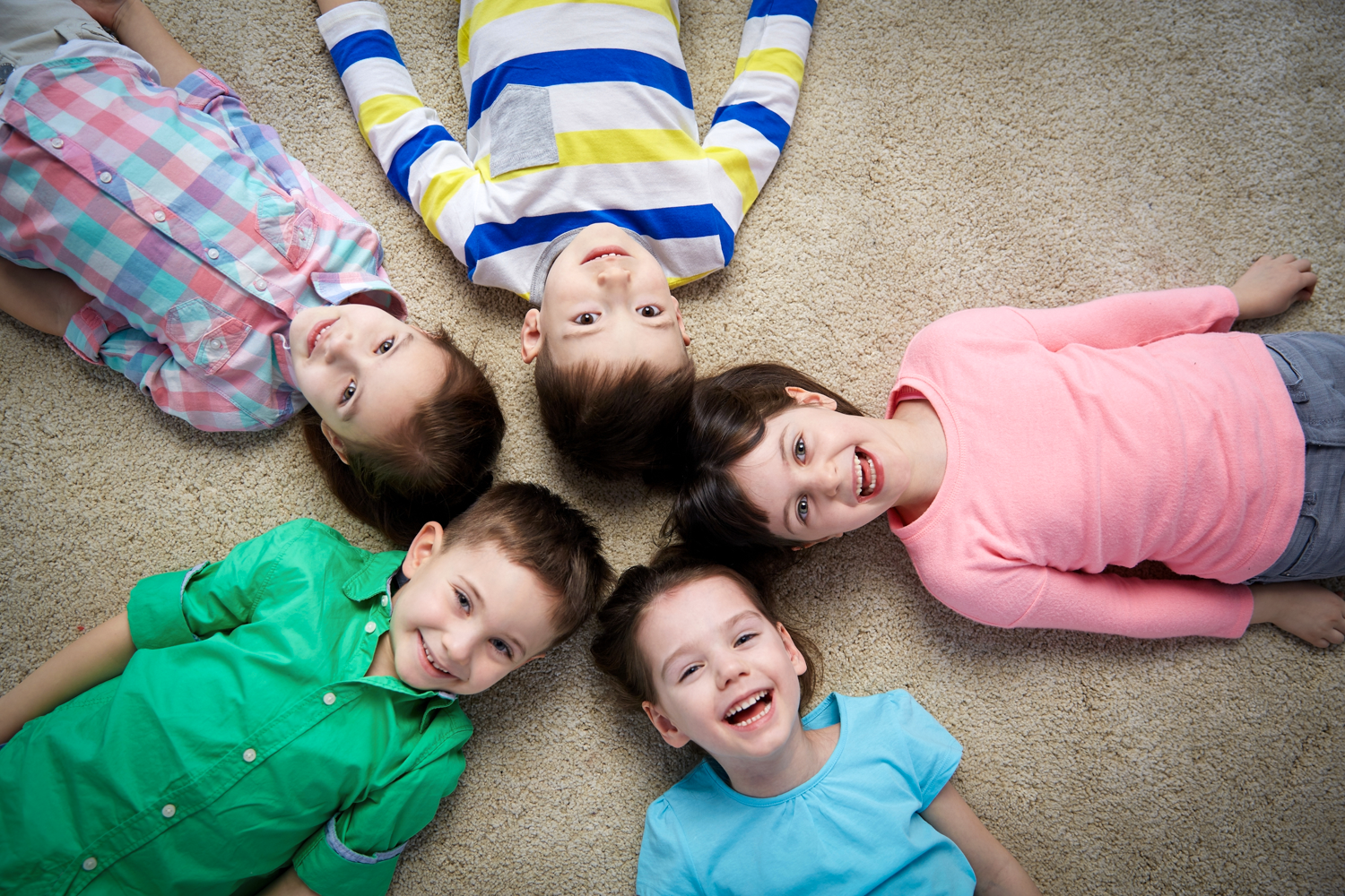 Five boys and girls laying flat on their backs laughing. A birds-eye view picture