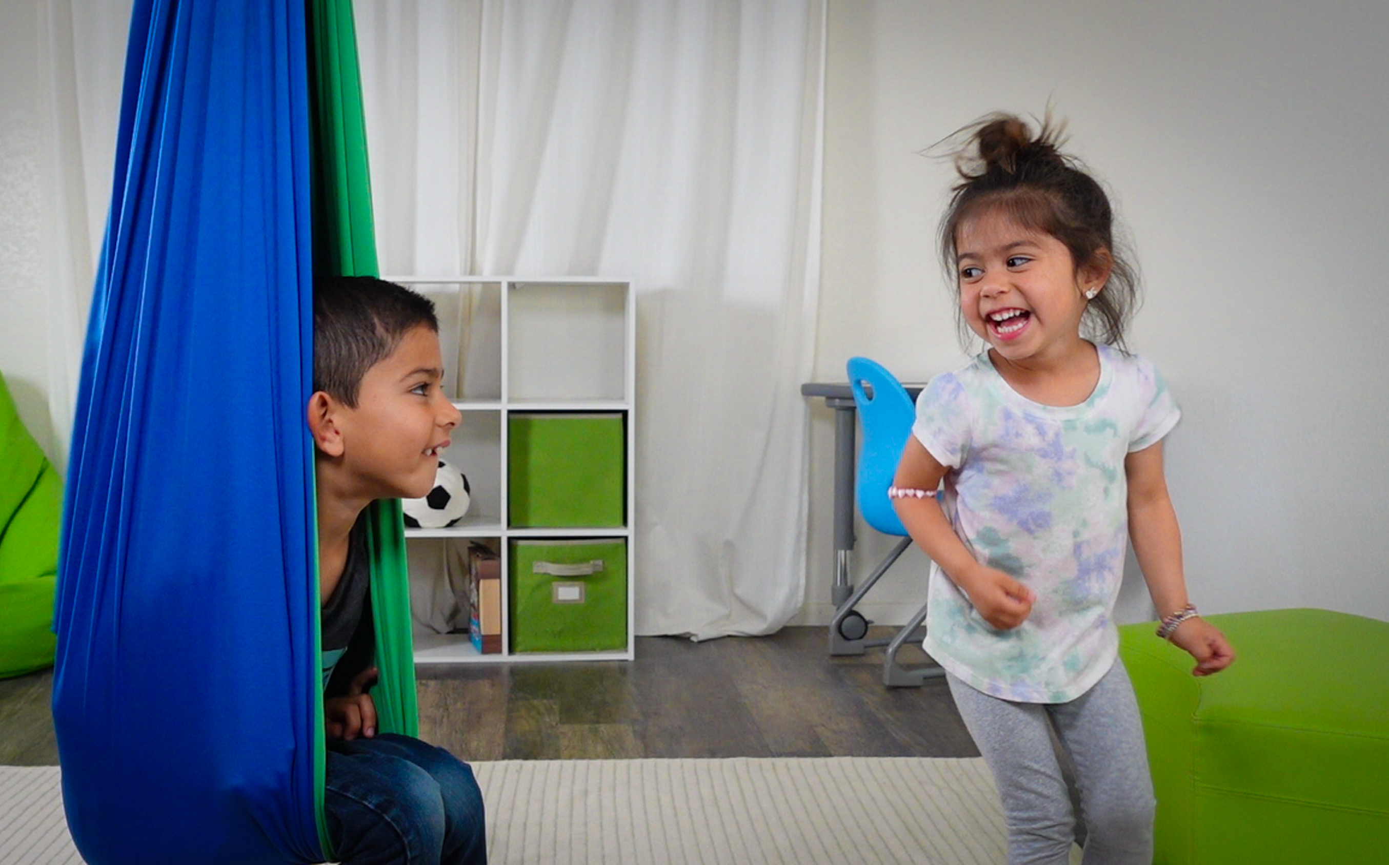 Two kids playing and one is sitting on a sensory swing